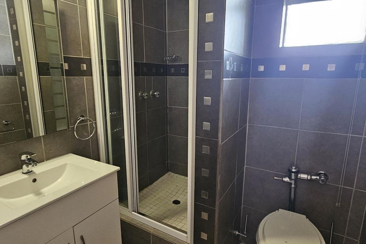 A modern bathroom featuring dark wall tiling, a vanity cabinet with a basin, a glass-enclosed shower, and a flush toilet.