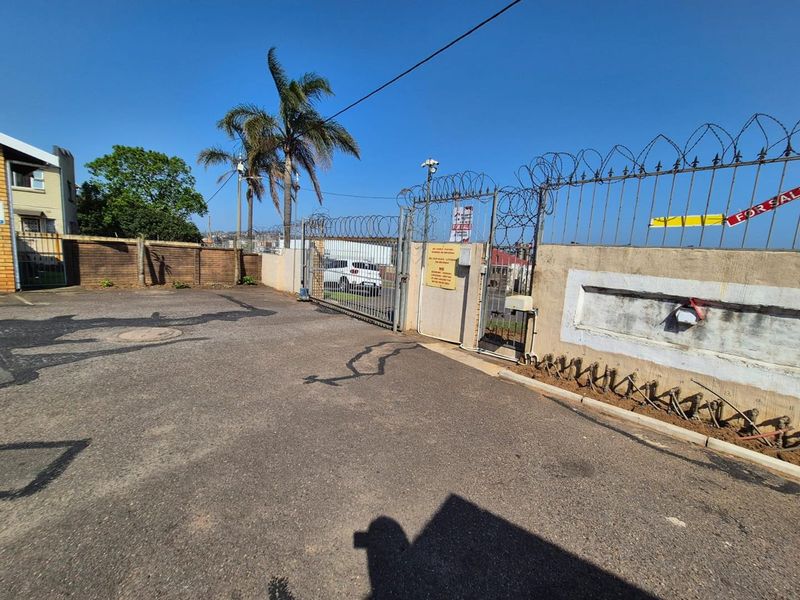 Front exterior view of the property featuring a paved driveway, secure gated entrance, and perimeter walling with security fencing.