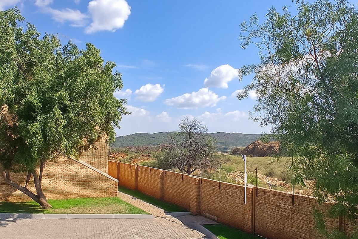 A view of the property exterior featuring a paved driveway, brick boundary wall, and landscaped garden area with scenic mountain views in the background.
