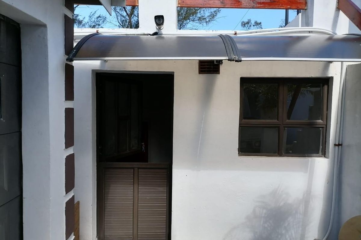 Rear exterior view showing a stable door, aluminium window, and a protective polycarbonate awning with a mounted security camera.