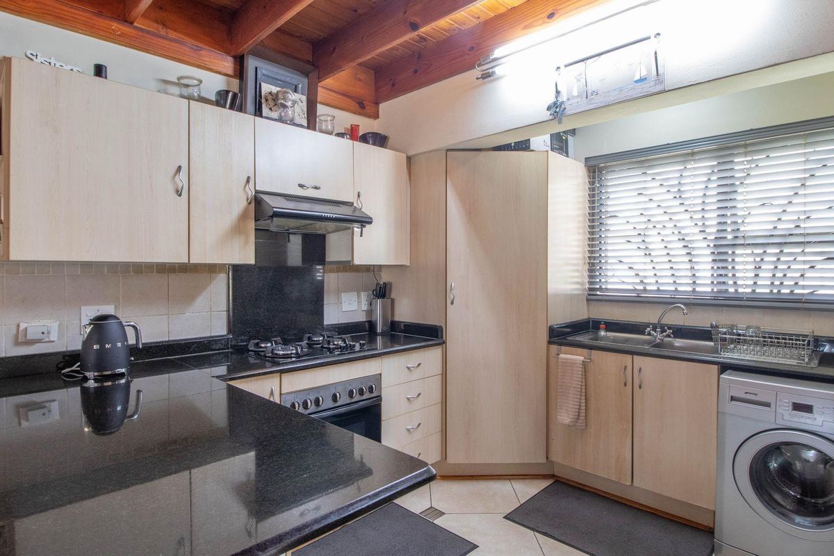 A functional kitchen featuring light wood-tone cabinetry, black granite countertops, a built-in oven with gas hob, and an integrated laundry appliance space.