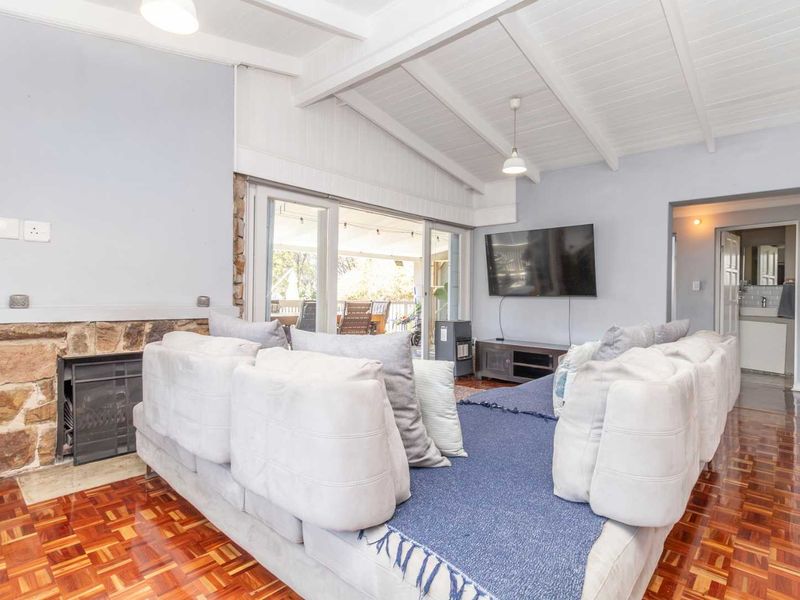 Spacious living room featuring a stone fireplace, classic parquet flooring, and exposed beam ceilings with direct access to an outdoor patio area.