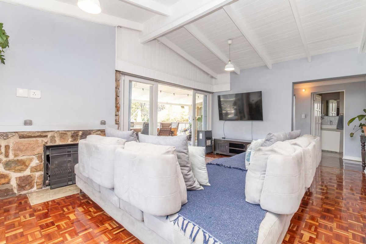 Spacious living room featuring a stone fireplace, classic parquet flooring, and exposed beam ceilings with direct access to an outdoor patio area.