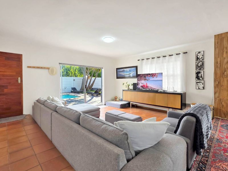 Spacious living room featuring terracotta floor tiles and a large sliding glass door providing direct access to the outdoor pool area.