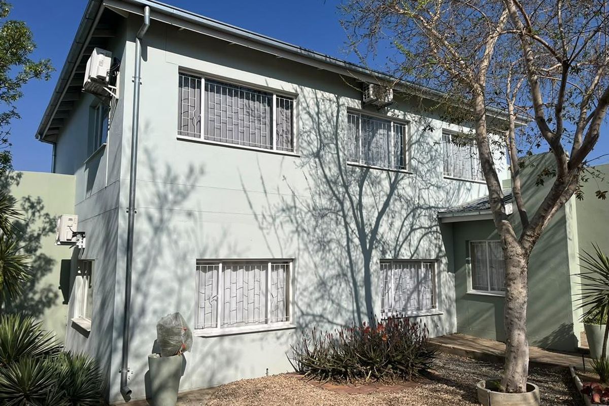 Rear elevation of a two-story townhouse featuring light-colored exterior walls, security bars on windows, and external air conditioning units.