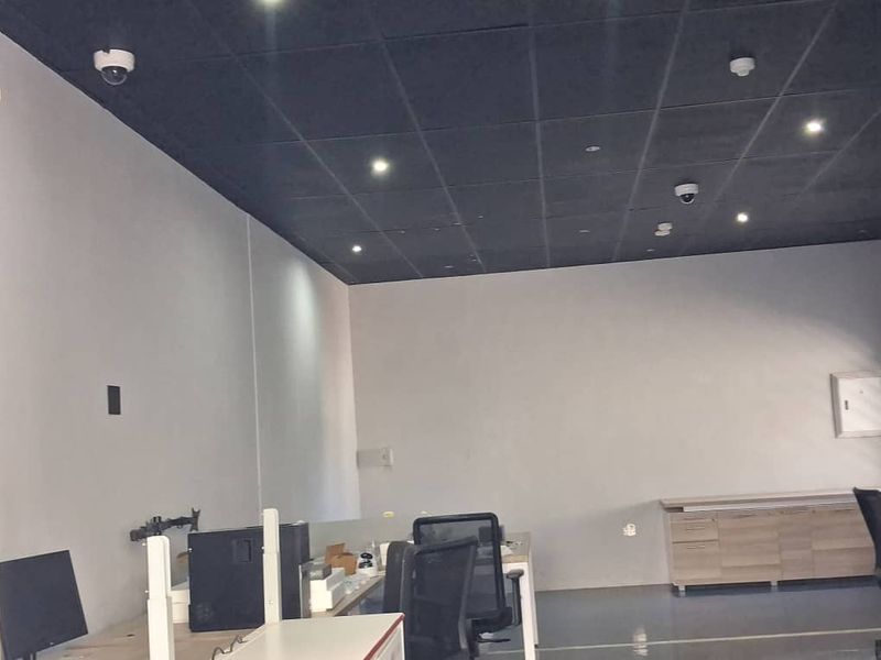 A functional office space featuring a dark suspended ceiling with recessed lighting, security cameras, and built-in storage cabinetry.