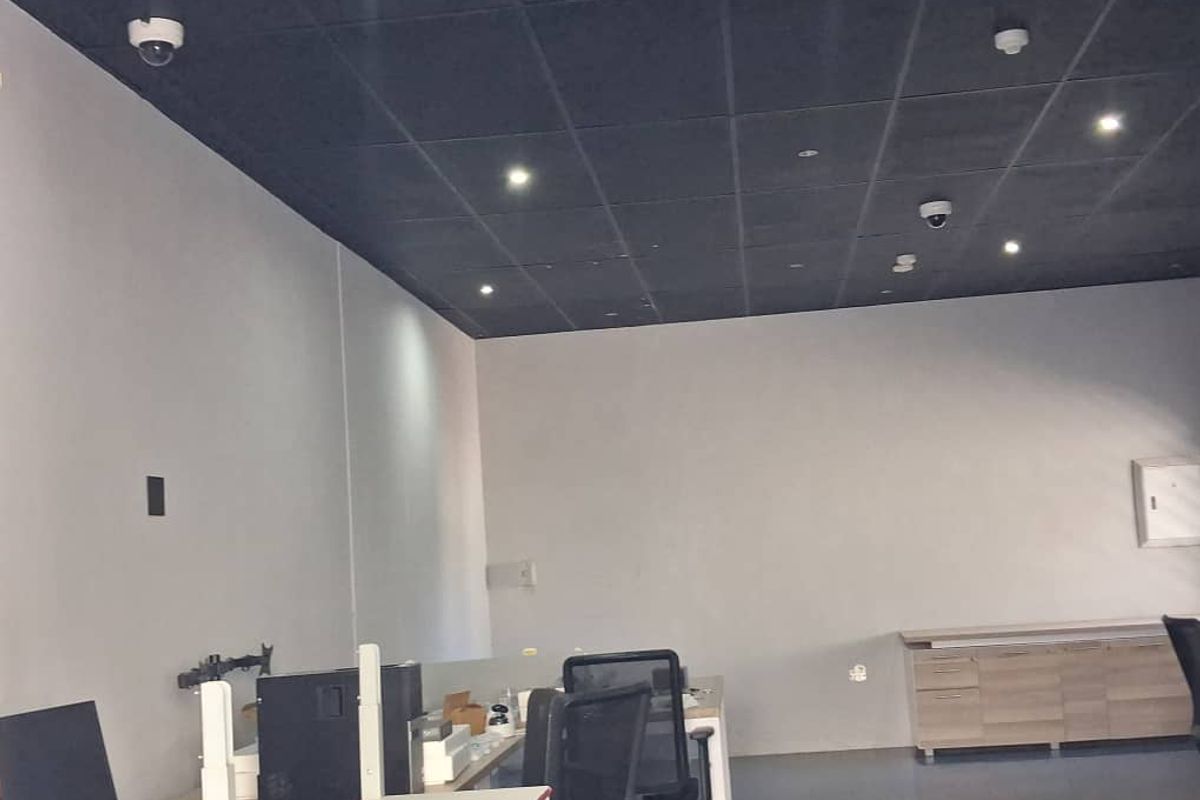 A functional office space featuring a dark suspended ceiling with recessed lighting, security cameras, and built-in storage cabinetry.