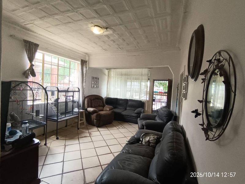 A living room featuring tiled flooring and decorative ceiling tiles, offering a spacious layout with natural light from large windows.