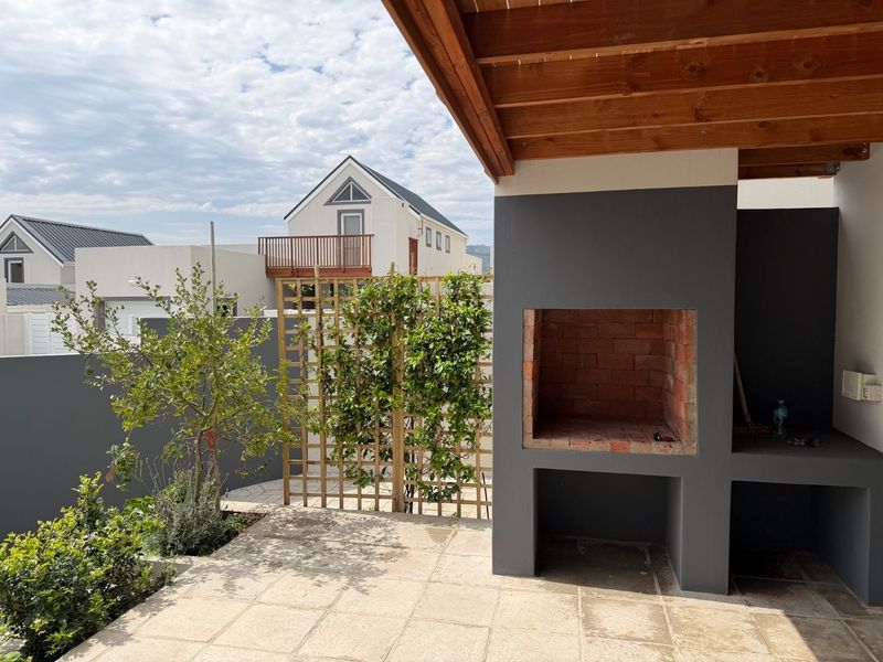 Covered patio area featuring a built-in brick braai, timber ceiling, and paved flooring, overlooking a landscaped garden space.