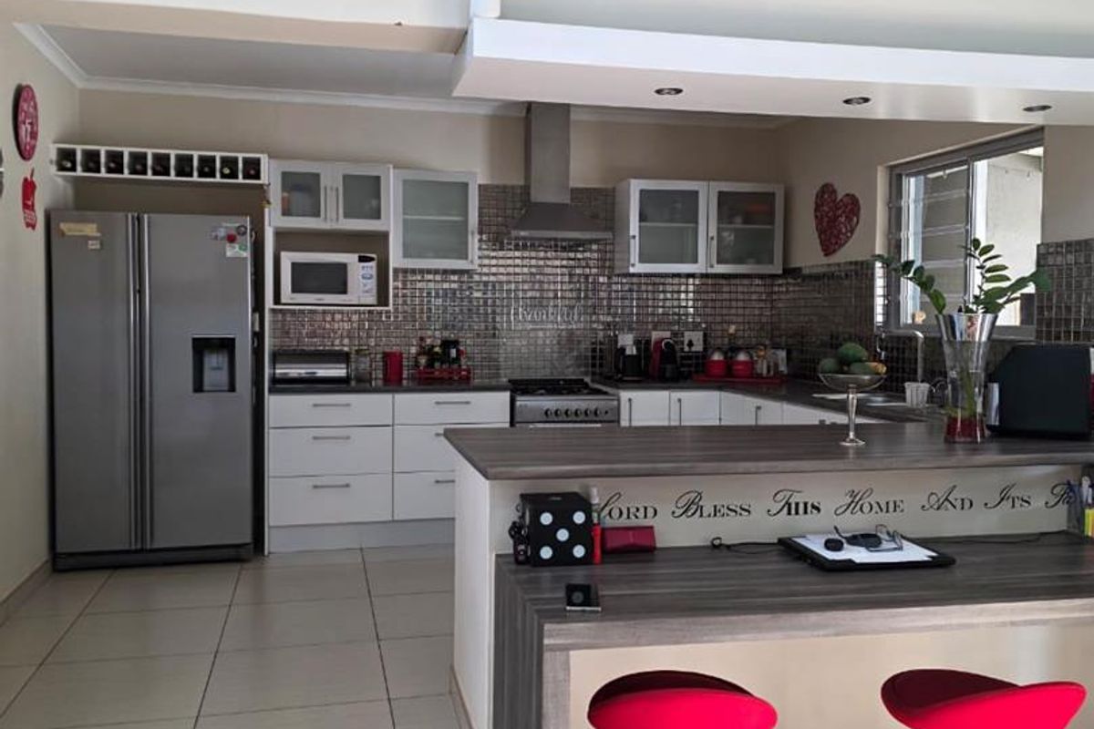A functional kitchen featuring modern cabinetry, a stainless steel extractor fan, tiled splashback, and a convenient breakfast bar area with tiled flooring.