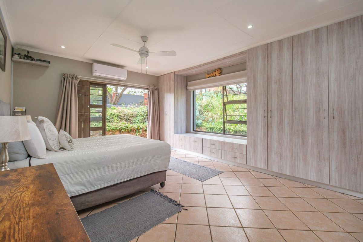 Spacious bedroom featuring built-in cupboards, a window seat, tiled flooring, ceiling fan, and air conditioning with direct access to the garden.