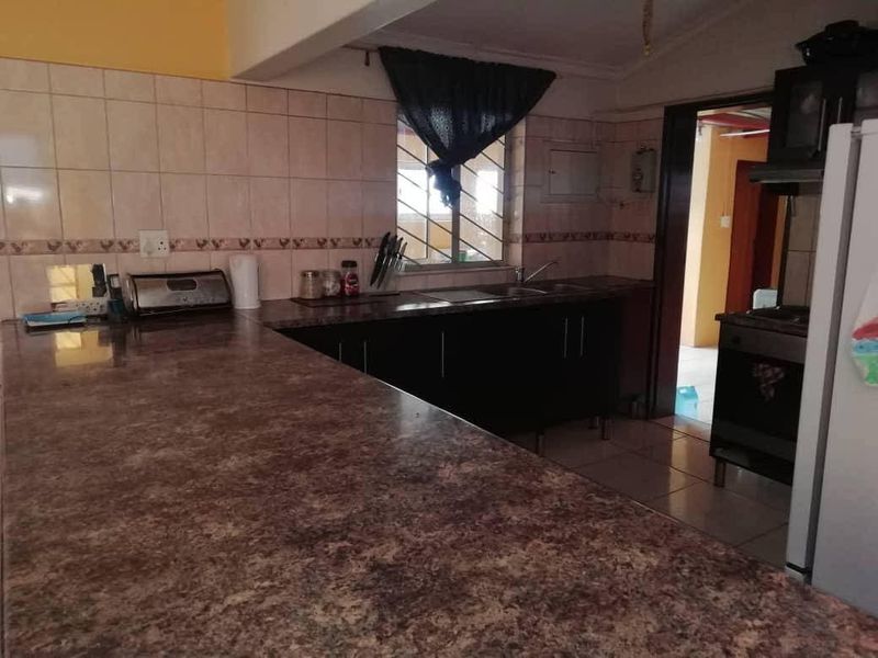 Functional kitchen featuring laminate countertops, tiled backsplash, built-in cabinetry, and tiled flooring with a view into the adjacent room.