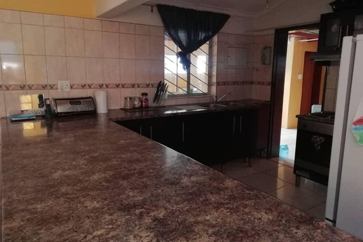 Functional kitchen featuring laminate countertops, tiled backsplash, built-in cabinetry, and tiled flooring with a view into the adjacent room.