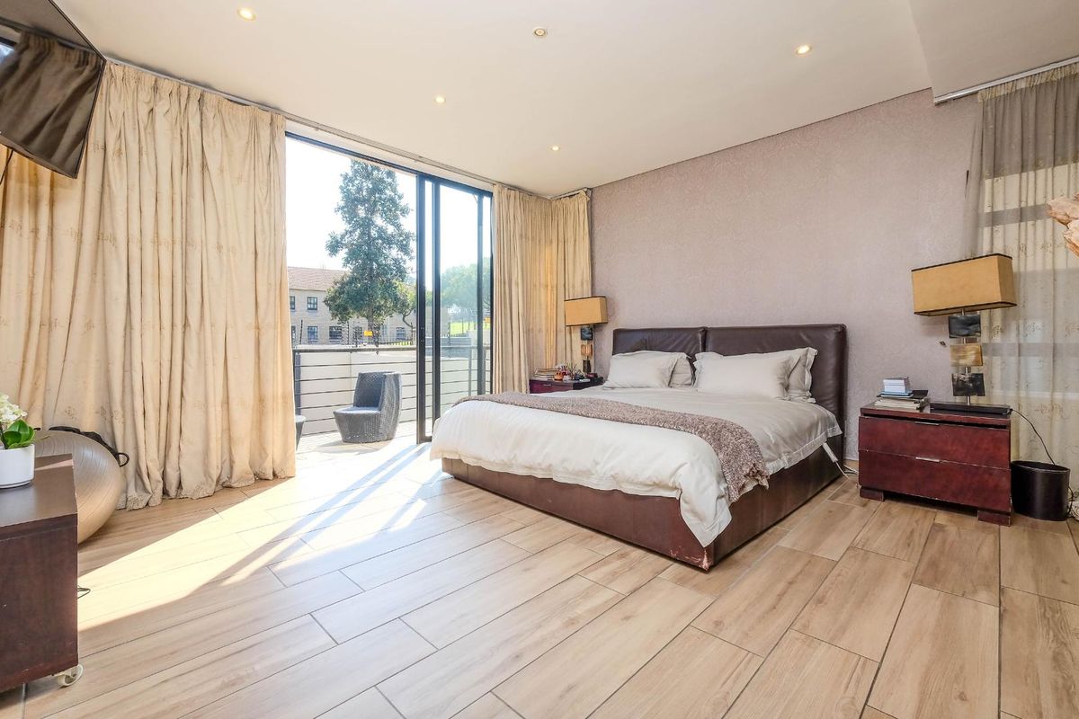 Spacious bedroom featuring wood-look tile flooring, recessed lighting, and large sliding glass doors opening onto a private balcony.