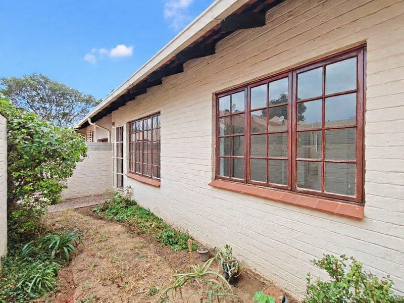 A view of the rear exterior facade featuring painted brick walls, timber-framed windows, and exposed rafter tails with an adjacent garden area.