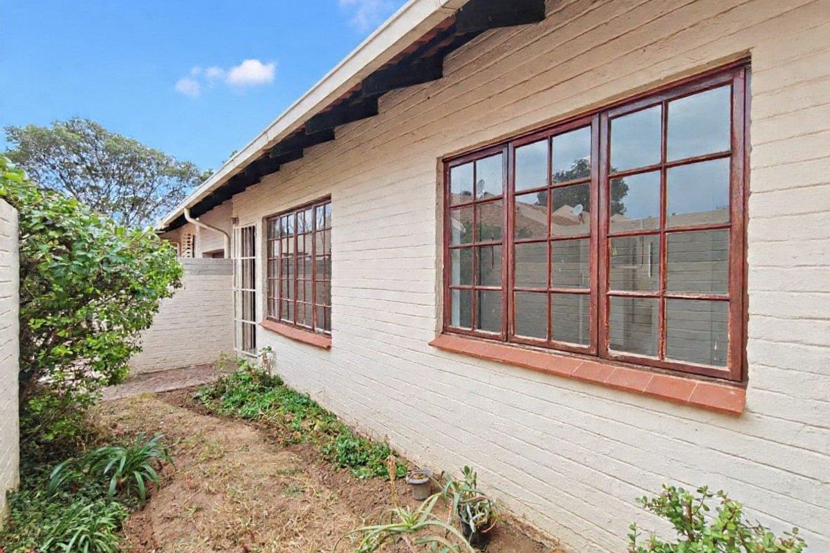 A view of the rear exterior facade featuring painted brick walls, timber-framed windows, and exposed rafter tails with an adjacent garden area.