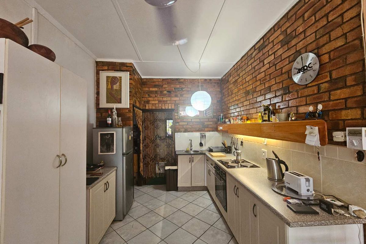 A functional galley-style kitchen featuring exposed brick walls, tiled flooring, built-in cabinetry, and integrated cooking appliances.