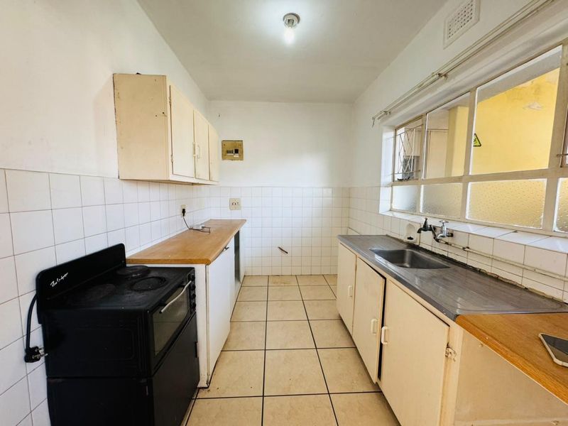 A functional, empty kitchen featuring tiled flooring, built-in cabinetry, a stainless steel sink, and an electric stove, ready for renovation or modernization.