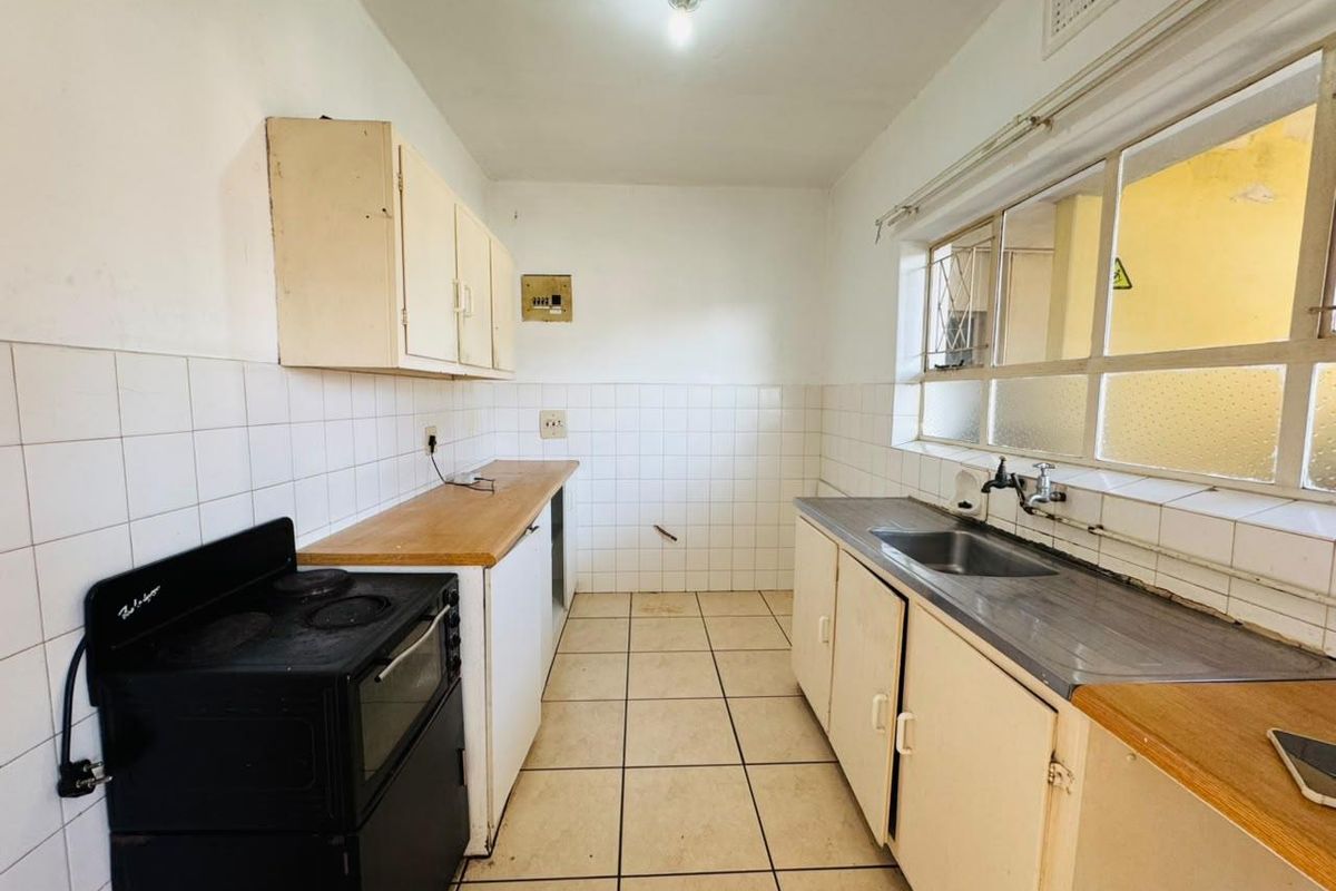 A functional, empty kitchen featuring tiled flooring, built-in cabinetry, a stainless steel sink, and an electric stove, ready for renovation or modernization.