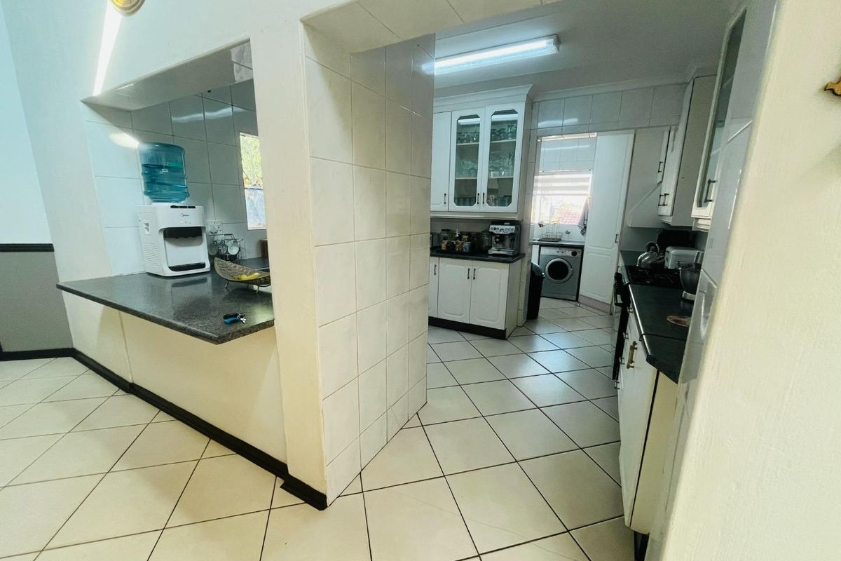 A functional kitchen and scullery area featuring tiled flooring, built-in cabinetry, and a breakfast counter, providing practical workspace and storage.