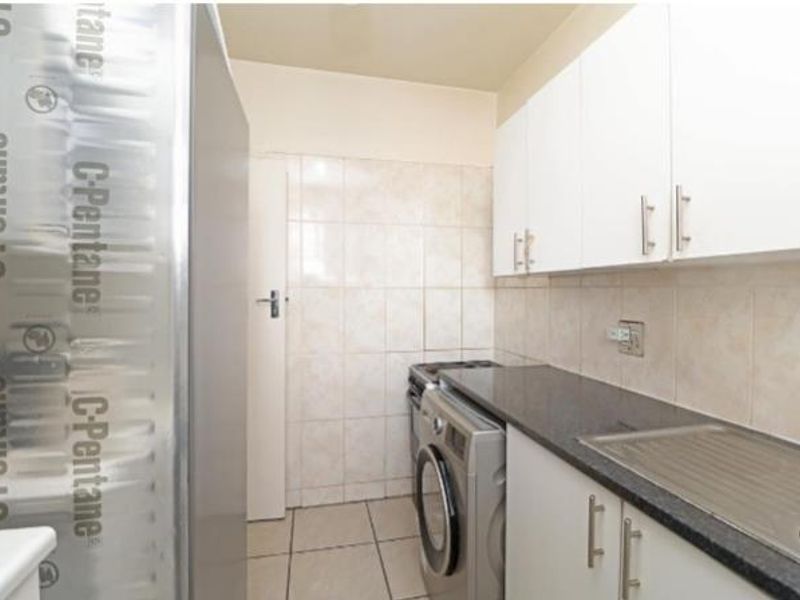 A functional kitchen featuring white cabinetry, dark stone countertops, tiled backsplash, and integrated laundry appliance space.