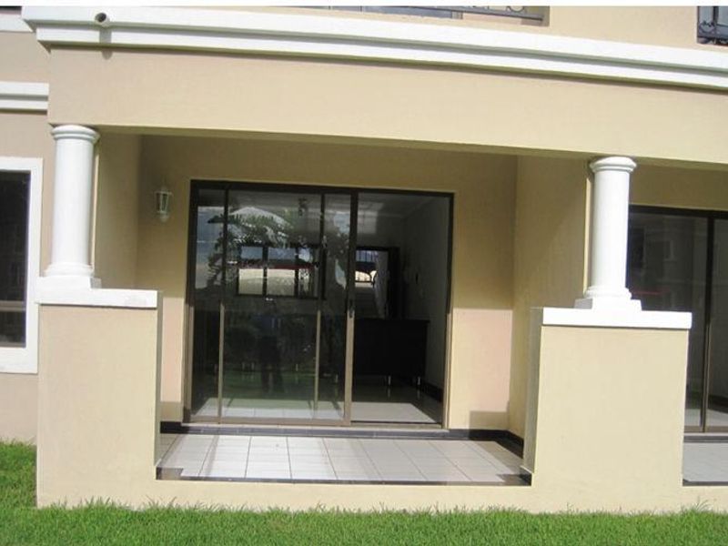 A covered ground-floor patio featuring tiled flooring, decorative columns, and sliding glass doors providing access to the interior living space.
