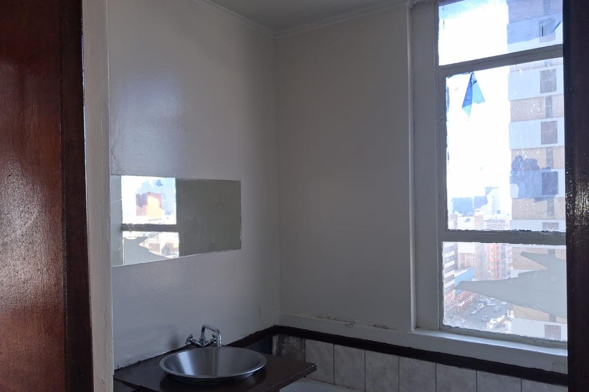 A small bathroom area featuring a stainless steel basin, tiled splashback, and a large window with visible damage to the glass and frame.