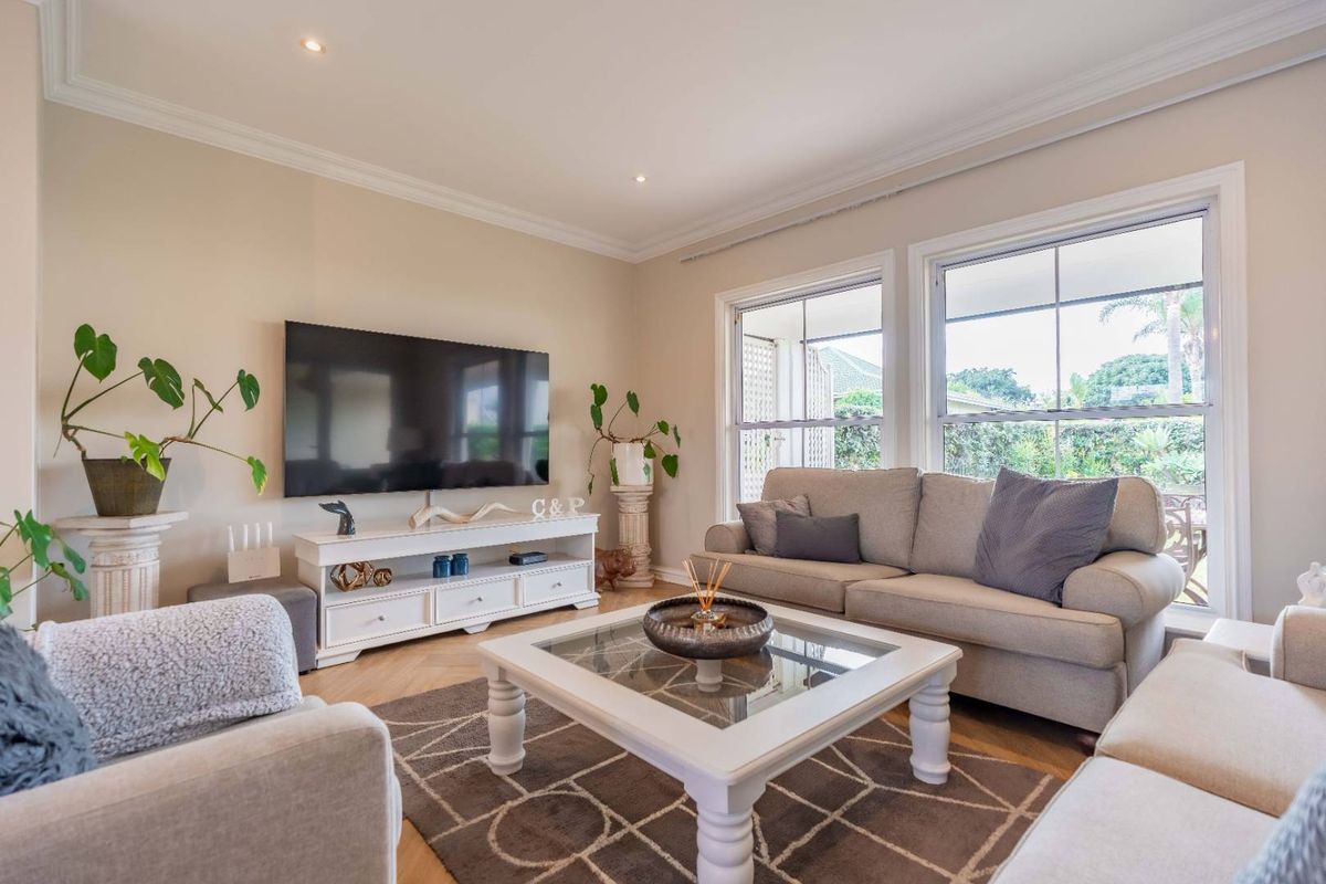 A bright and well-maintained living room featuring hardwood flooring, crown molding, and large windows that provide ample natural light.