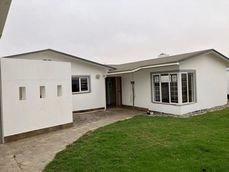 Rear exterior view of the house featuring a paved patio area, a prominent bay window, and a well-maintained lawn.