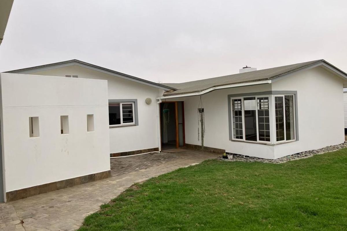 Rear exterior view of the house featuring a paved patio area, a prominent bay window, and a well-maintained lawn.