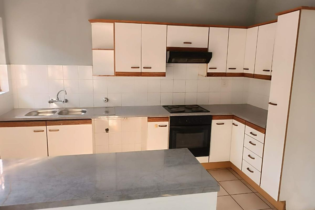 A functional kitchen featuring white cabinetry with wood trim, a built-in oven, hob, extractor fan, and a double sink with tiled splashbacks.