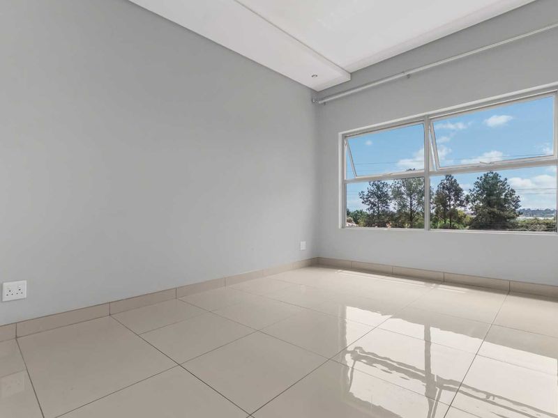 A bright and spacious empty bedroom featuring neutral tiled flooring, built-in cupboards, and large windows offering natural light and pleasant outdoor views.