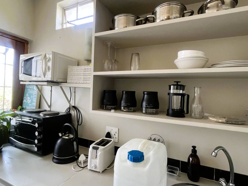 A compact kitchen area featuring built-in open shelving, a sink with faucet, and a tiled backsplash, providing functional prep and storage space.