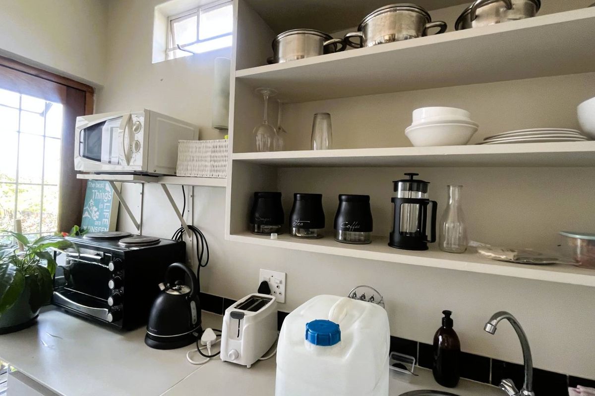 A compact kitchen area featuring built-in open shelving, a sink with faucet, and a tiled backsplash, providing functional prep and storage space.