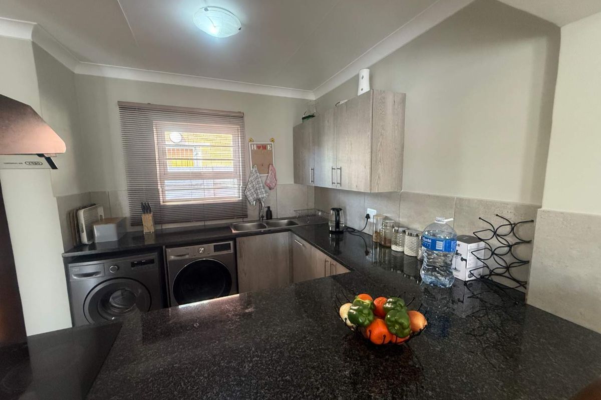 A functional kitchen featuring dark granite countertops, light wood-finish cabinetry, a double sink, and a built-in extractor fan with a tiled backsplash.