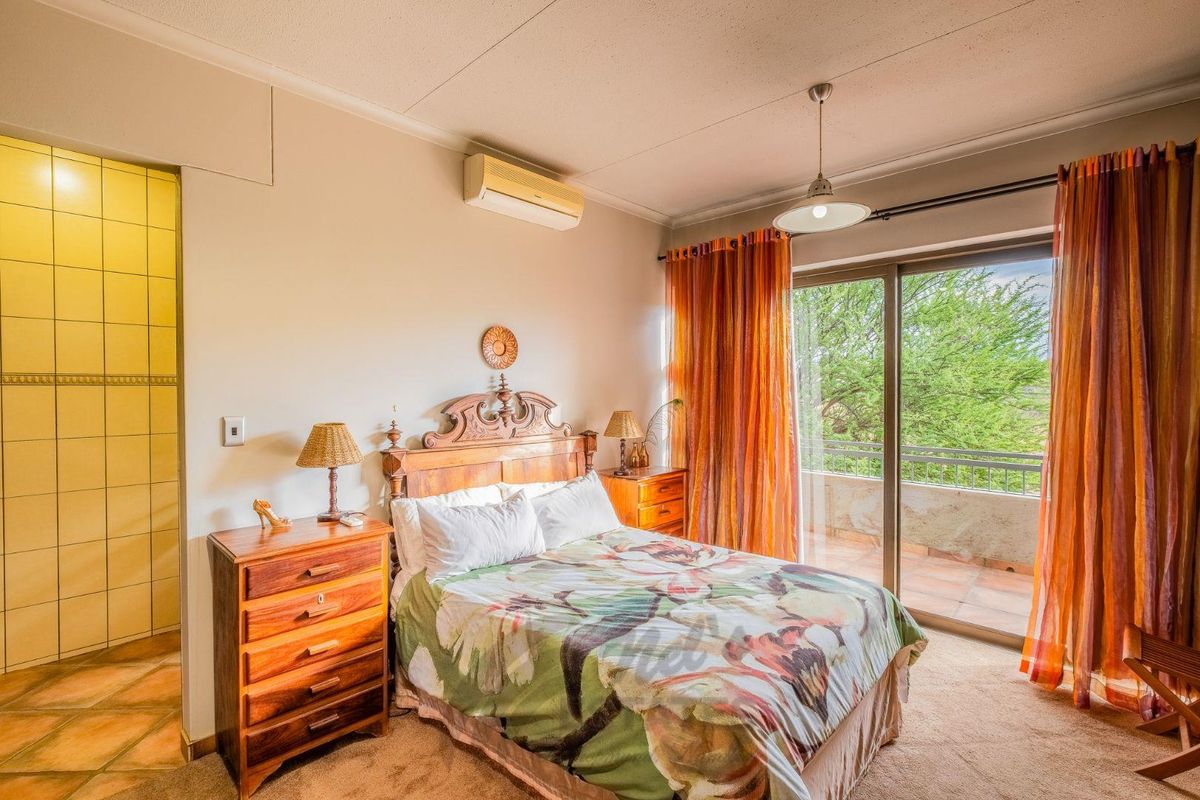 A bedroom featuring a wall-mounted air conditioning unit, sliding glass doors leading to a private balcony, and an adjoining tiled en-suite bathroom.