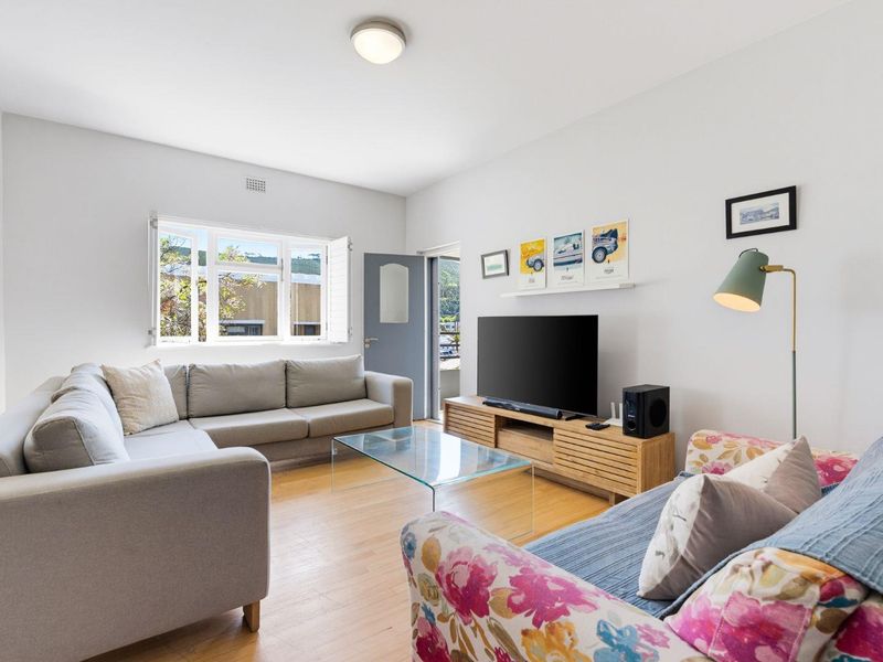 A bright and well-maintained living room featuring timber flooring, a large casement window, and neutral wall finishes.