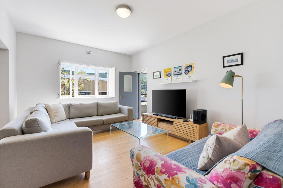 A bright and well-maintained living room featuring timber flooring, a large casement window, and neutral wall finishes.