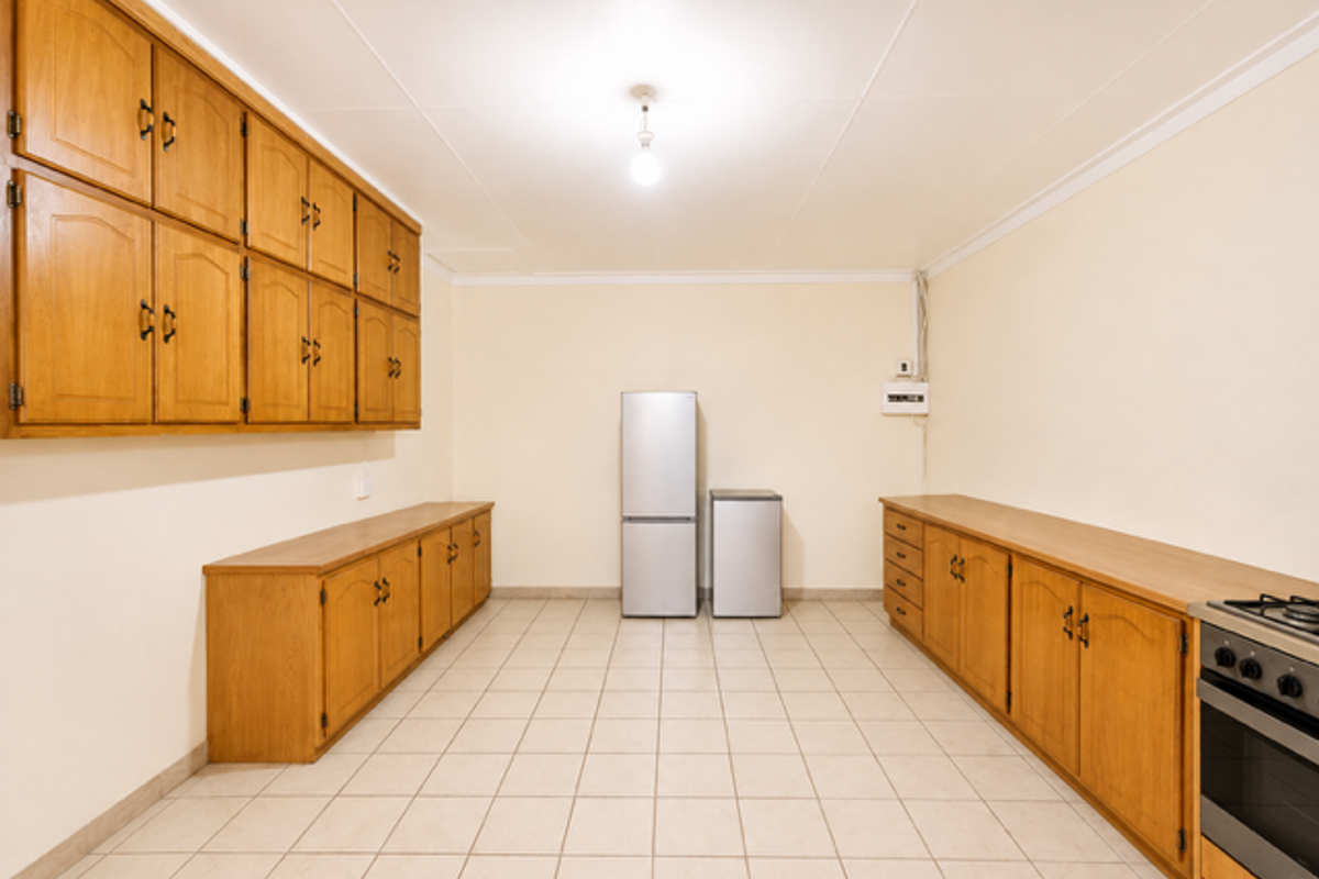 Spacious kitchen featuring extensive wooden cabinetry, tiled flooring, and a built-in oven and hob, offering ample storage and workspace.