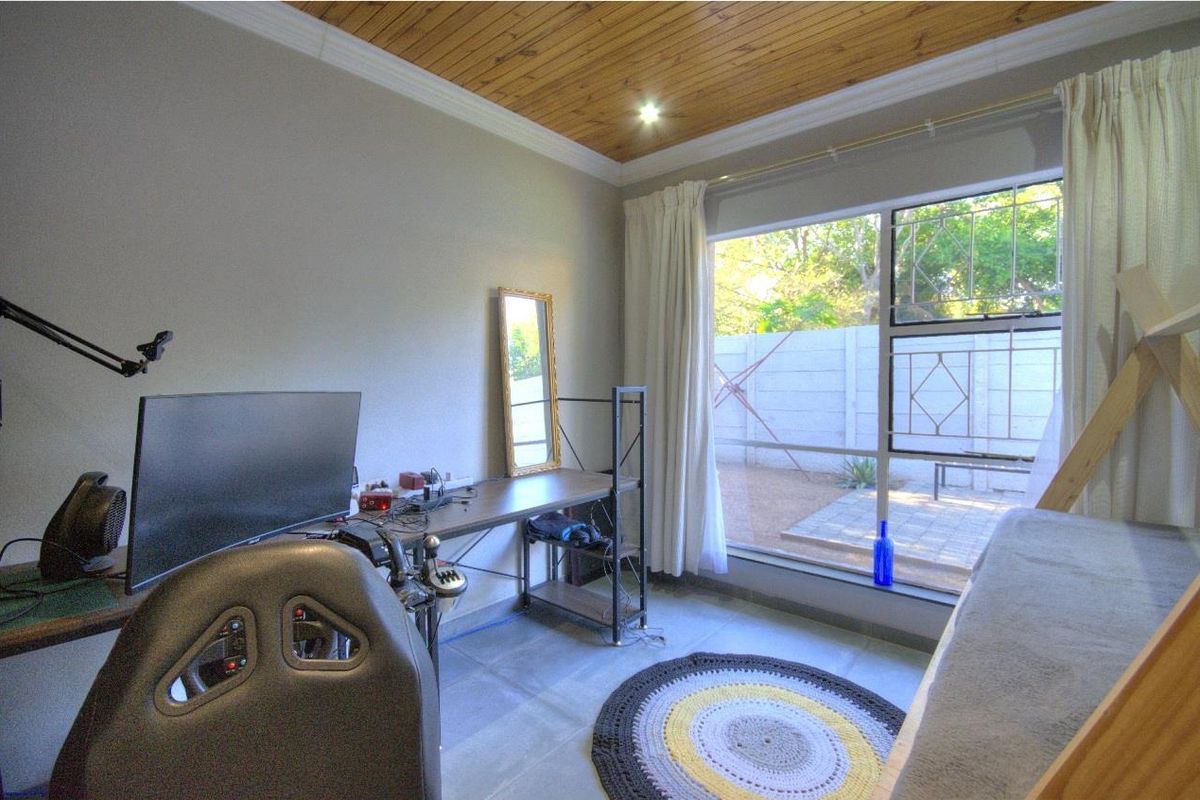 A bedroom featuring tiled flooring, a timber-paneled ceiling, and a large window providing natural light and garden views.