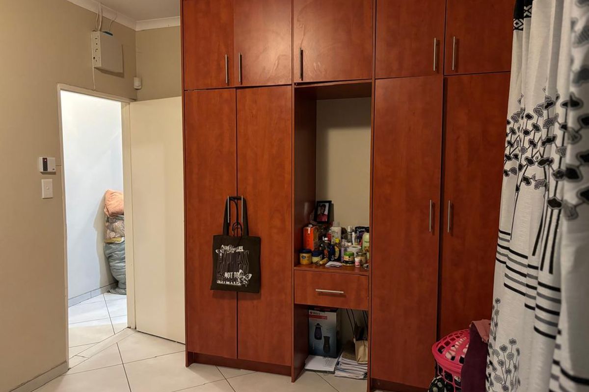 A bedroom featuring built-in wooden cabinetry with integrated shelving and storage, finished with tiled flooring and a doorway leading to an adjacent space.