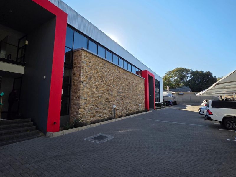 Modern office building exterior featuring a striking stone facade, red architectural accents, and a paved parking area with covered carports.
