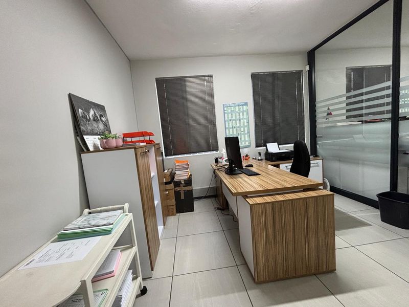 A functional office space featuring tiled flooring, venetian blinds, and a modern glass partition wall, providing a professional work environment.