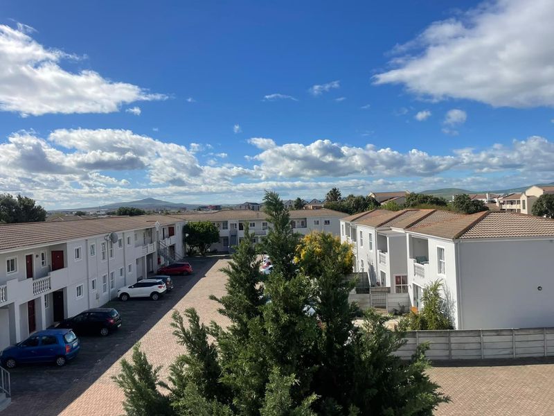 An elevated view of the apartment complex grounds, featuring paved parking areas, multi-story residential blocks with tiled roofs, and landscaped surroundings.