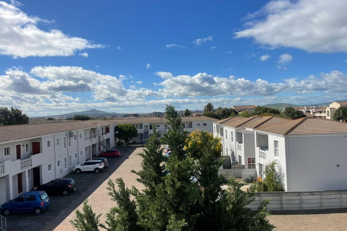 An elevated view of the apartment complex grounds, featuring paved parking areas, multi-story residential blocks with tiled roofs, and landscaped surroundings.