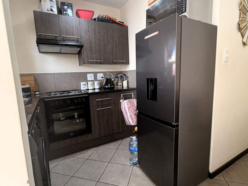 Compact kitchen featuring dark wood cabinetry, granite countertops, built-in oven with hob, extractor fan, and tiled flooring.