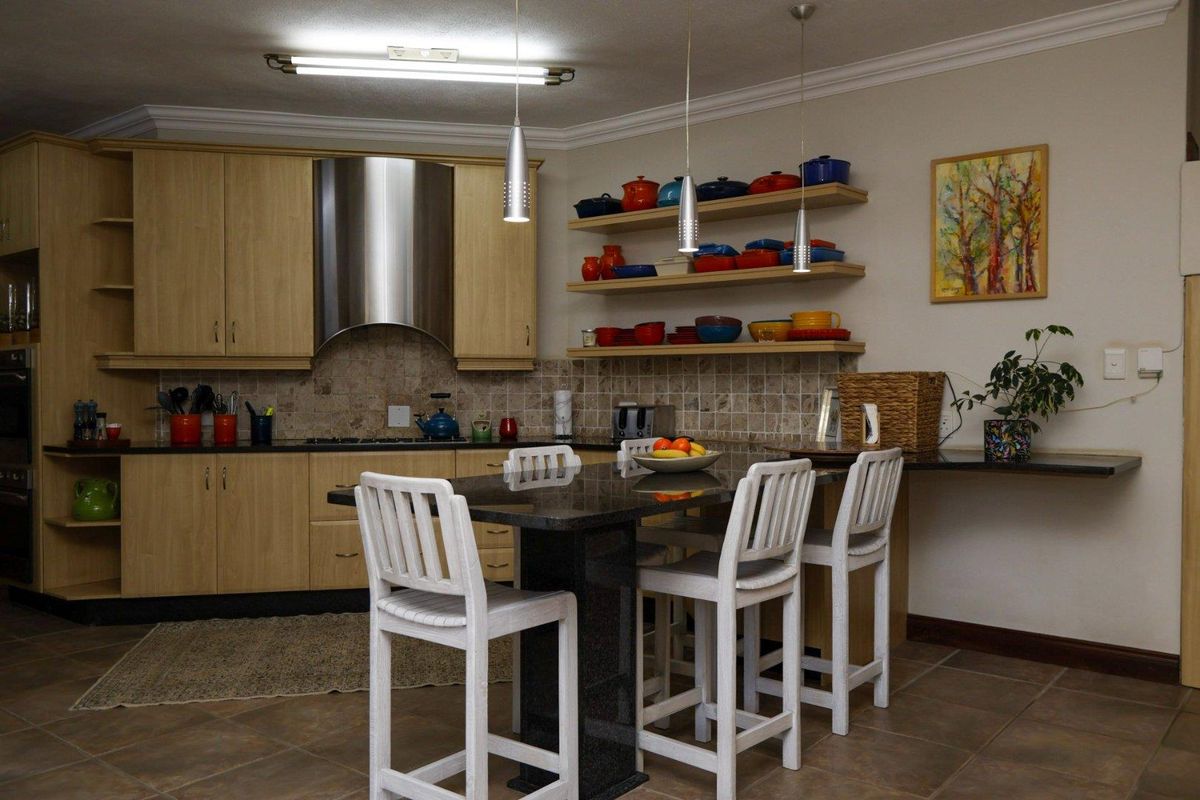 A functional kitchen featuring light wood cabinetry, granite countertops, a stainless steel extractor fan, and a built-in breakfast bar with tiled flooring.