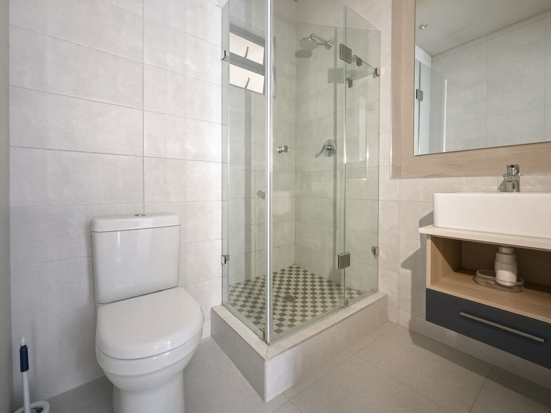 Modern bathroom featuring a glass-enclosed shower, wall-mounted vanity with vessel sink, and neutral tiled finishes throughout.