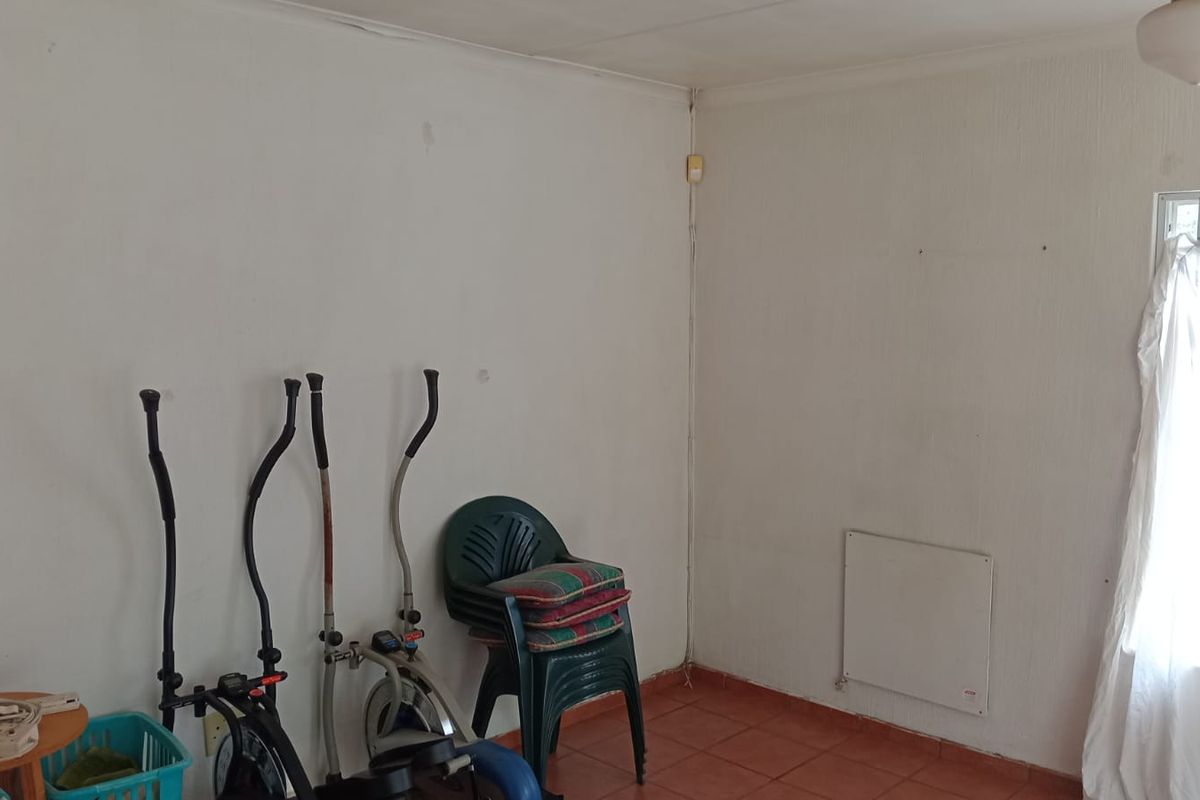 A simple interior room featuring tiled flooring, a wall-mounted heater, and a window with security bars.