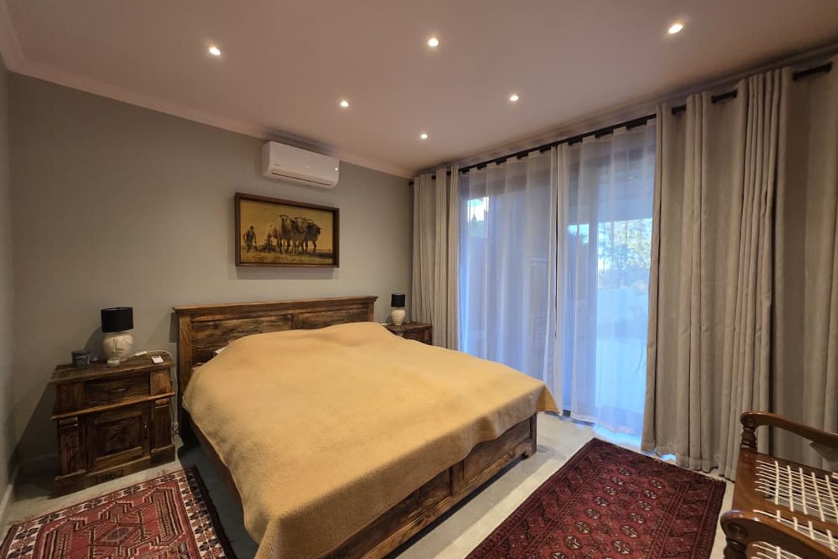A well-maintained bedroom featuring recessed ceiling lighting, a wall-mounted air conditioning unit, and large sliding glass doors leading to an outdoor area.
